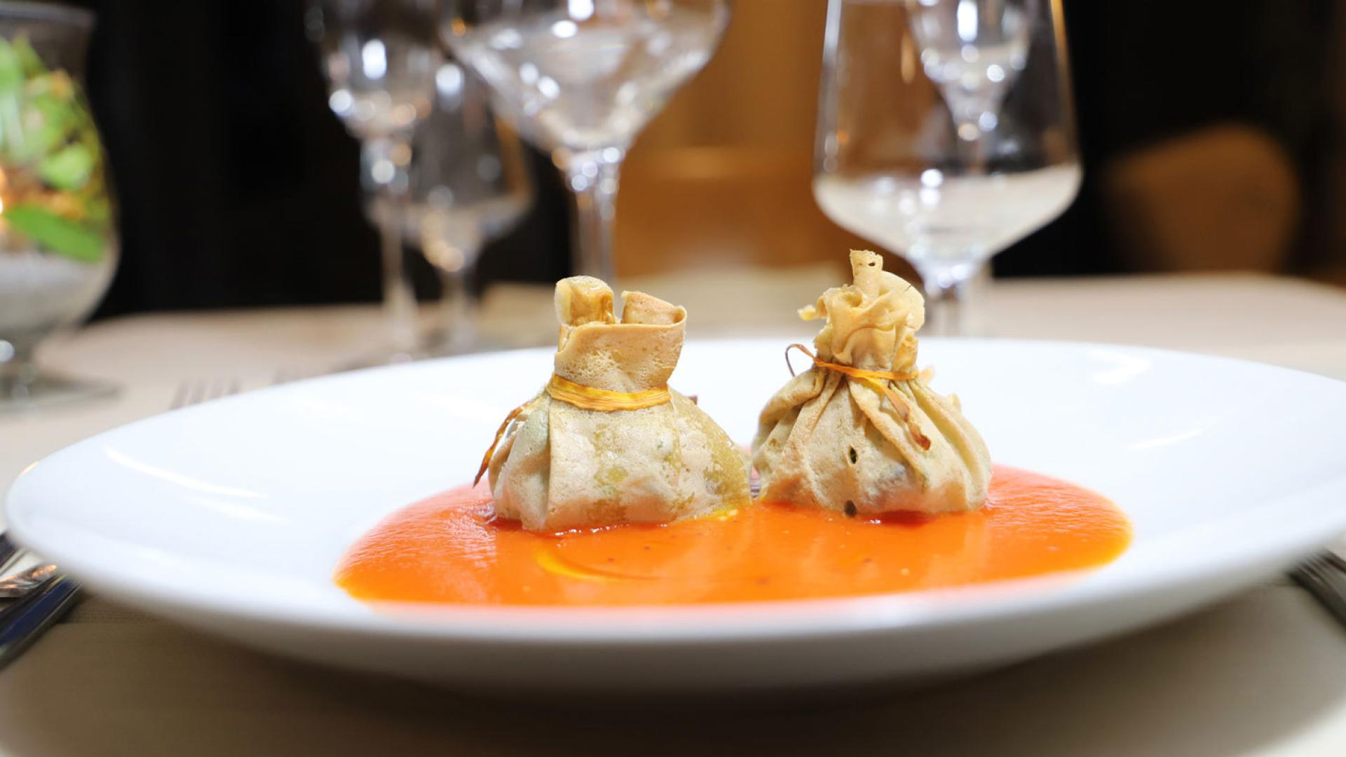 Fagottini su crema di pomodoro, presentazione elegante in un ristorante raffinato.