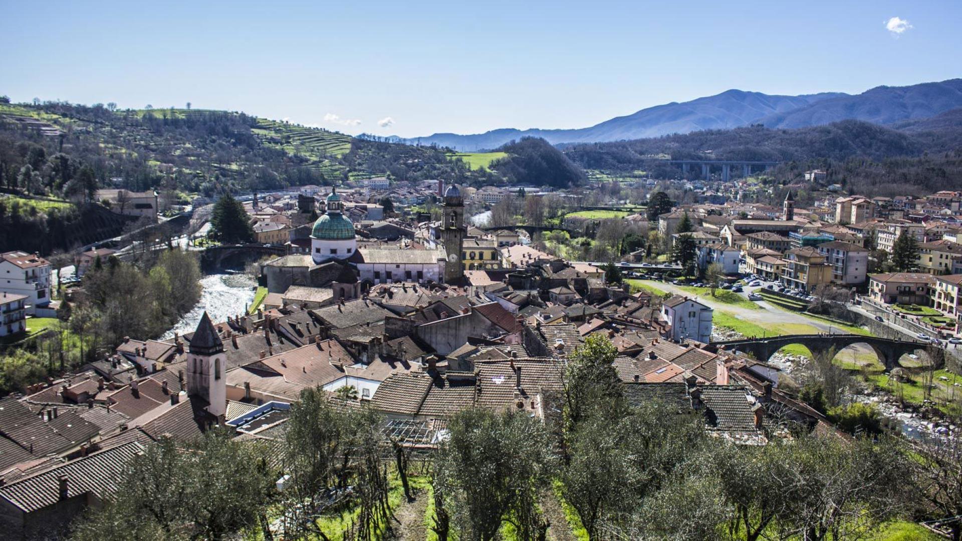 Vista panoramica di un borgo italiano con colline, fiume e ponte storico.