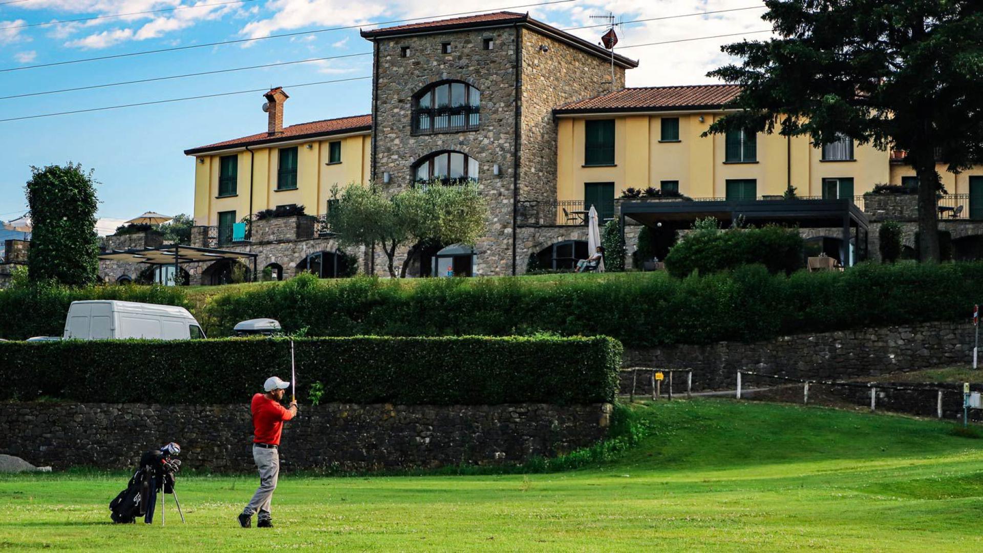 Golfista in azione davanti a un edificio in pietra e campagna verde.