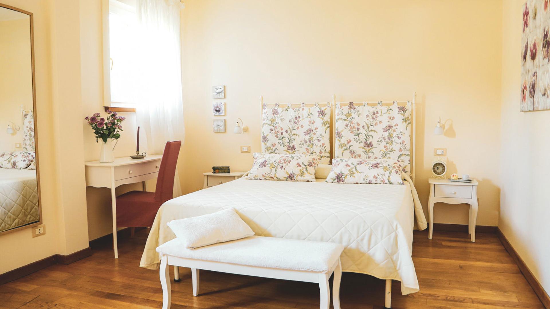 Camera da letto luminosa con arredi floreali e mobili bianchi eleganti.
