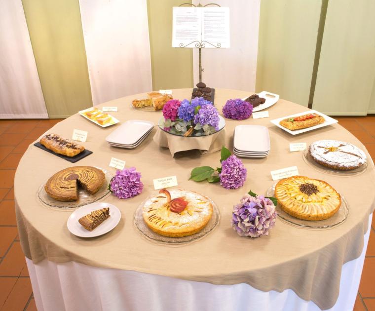 Tavolo con dolci assortiti, fiori di ortensia e cartellini descrittivi.