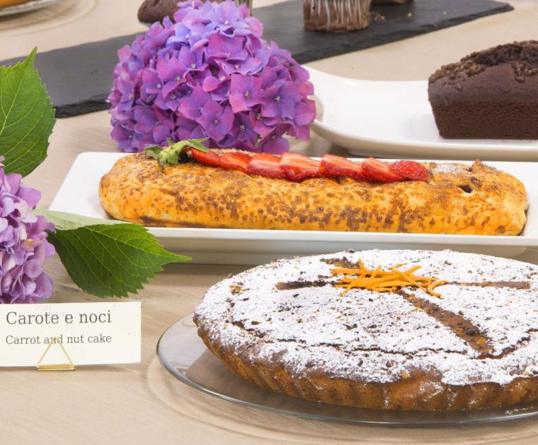 Dolci assortiti: torta al cioccolato, torta agli amaretti, carote e noci, decorazioni floreali.