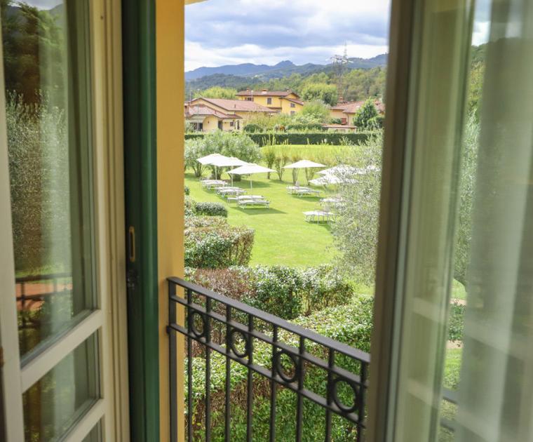 Vista su giardino verde con ombrelloni e sdraio, montagne sullo sfondo.