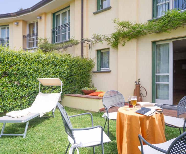Giardino con sedie, tavolo apparecchiato e sdraio davanti a una casa.