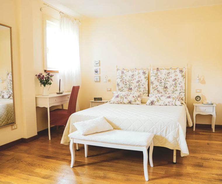 Camera accogliente con letto matrimoniale, arredi floreali e legno chiaro.